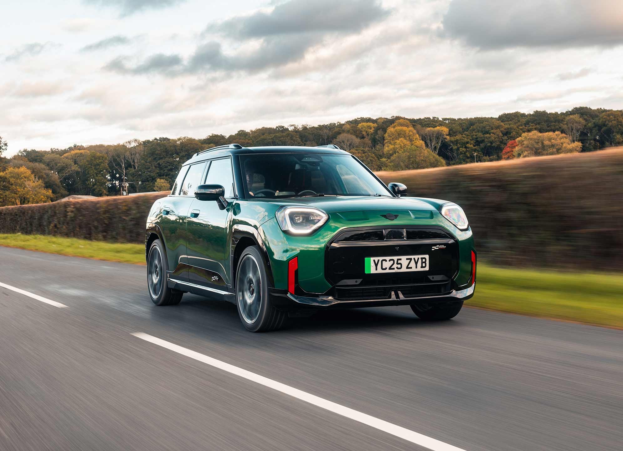 Front view of parking all-electric MINI Aceman in British Racing Green in car park with pink wall in the background